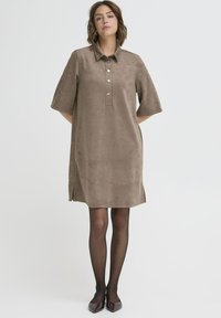 Brązowa sukienka z kołnierzykiem, wykonana z miękkiego materiału, z krótkimi rękawami, z zapięciem na guziki, bocznymi rozcięciami i luźnym krojem.