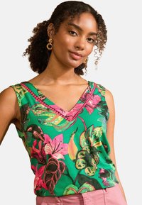 Žalias gėlių raštas V formos kaklo marškinėliai, su ryškiomis rožinėmis ir geltonomis detalėmis; turi tekstūruotą detalę aplink kaklą.