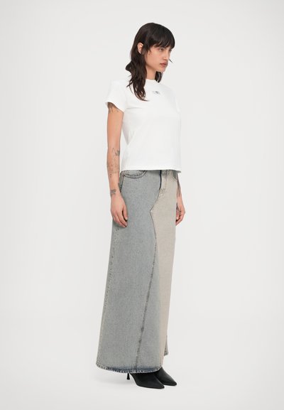 Biele bavlnené tričko s okrúhlym výstrihom, skombinované s dlhou dvojfarebnou džínsovou sukňou so stranovým švom a neupraveným lemom. Čierne čižmy na podpätku.