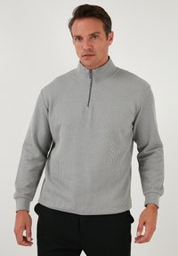 Gray ribbed pullover with a high neck and partial zipper. Features long sleeves and a textured fabric for added dimension.
