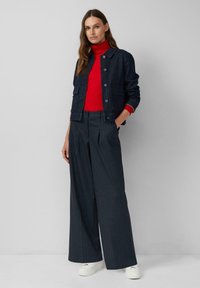 Ciemnoniebieska dżinsowa kurtka z guzikami, czerwona sweterek typu golf oraz szerokie spodnie w prążki. Całość dopełniają białe trampki.