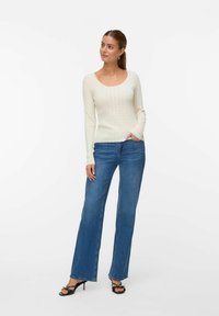 Roomkleurig, geribbelde langekorting top met een ronde hals, gecombineerd met lichtblauwe flared jeans en zwarte hakken sandalen.