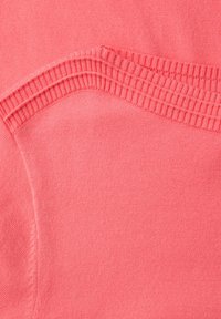 Zbliżenie różowego dzianego materiału ukazującego prążkowany dekolt i gładką fakturę swetra.