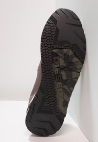 Brązowy sneaker z teksturowaną siateczkową cholewką, czarną gumową podeszwą i akcentami moro. Posiada głęboki bieżnik zapewniający przyczepność oraz logo na podeszwie.