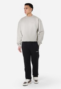 Grå sweatshirt med ribbede manchetter, parret med sorte sweatpants med et hvidt logo. Skoene er multitonede med en kraftig sål.