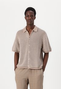 Beige knit short-sleeve shirt featuring a textured pattern and a light beige collar. The shirt has a relaxed fit and button closure.