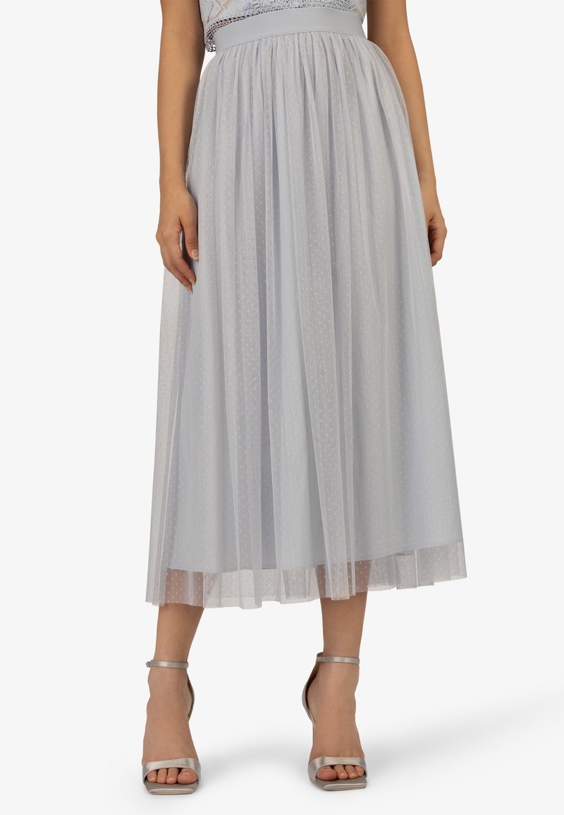 Jupe midi gris clair avec un overlay transparent à pois, froncée à la taille, portée avec des talons hauts argentés à bride cheville.