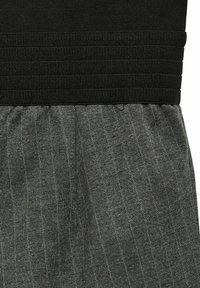 Cintura elástica negra con un diseño texturizado sobre una tela gris que presenta finas rayas verticales y sutiles acentos metálicos.