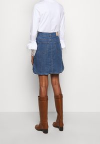 Jeans A-linje kjol i en blekt blå nyans, två bakfickor och en medellång design, kombinerad med en vit långärmad skjorta och bruna knähöga stövlar.