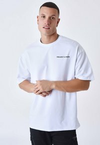 Witte katoenen t-shirt met een ronde hals en korte mouwen. Heeft zwarte tekst "PROJECT X PARIS" op de linkerkant van de borst. Vloeiende textuur.