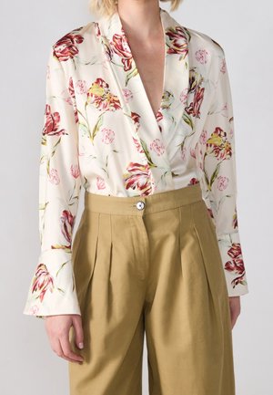 Biała bluzka z czerwono-żółtym kwiatowym wzorem, wkładana w spodnie z wysokim stanem, plisowane, beżowe, z zapięciem na guziki z przodu.