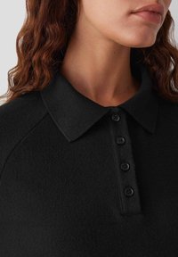 Polo shirt nera con colletto a costine, dotata di cinque bottoni neri sul davanti, realizzata in un tessuto strutturato.