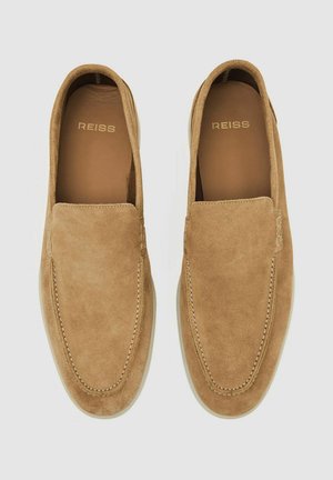 Brūni zamšādas slip-on apavi ar noapaļotu purngalu, kontrastējošu šuvju apdari un gludu iekšējo oderi. Redzams zīmola nosaukums "Reiss".