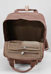 Ruskea kangaskassi, jossa on vetoketjuzus, avoin lokero ja etutasku. Teksturoitu sisäosa, jossa on verkko-yksityiskohtia ja vetoketjuja.