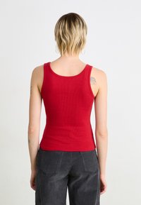 Top de tanque vermelho canelado com um design justo e alças largas, combinado com calças cinzas escuras de cintura alta.