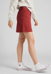 Falda de pana roja con corte recto, que presenta una cintura con una etiqueta, combinada con zapatillas altas blancas y una sudadera de color gris claro.