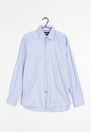 Chemise bleu clair à manches longues avec boutons, col et poignets, suspendue sur un cintre noir sur fond blanc.