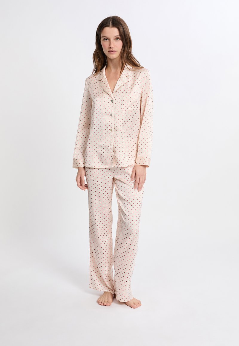 Conjunto de pijama de satén rosa claro con lunares rojos. Camisa de botones de manga larga con cuello y pantalones rectos a juego. Textura suave.