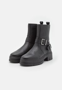 Black leather ankle boots with textured finish, wide strap and buckle detail, and chunky platform sole. Two pull tabs on the shaft.