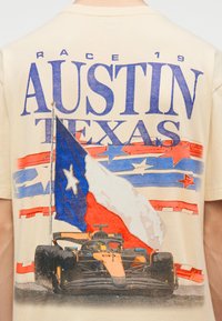 Πλάτη μπλουζάκι με θέμα αγώνων με το κείμενο "Austin Texas", τη σημαία του Τέξας σε κόκκινο, άσπρο και μπλε, και ένα γραφικό με αγωνιστικό αυτοκίνητο σε μαύρο και πορτοκαλί.