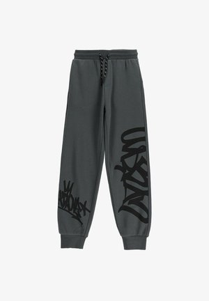 Ciemnoszare spodnie dresowe z czarnym nadrukiem w stylu graffiti na prawej udzie i lewej łydce, elastycznym pasem ze sznurkiem oraz ściągaczami przy kostkach.