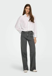 Hallide lai püksid ja valge nööbiga särk. Särgil on mugav lõige ja pikad varrukad. Pükstel on klassikaline viie taskuga disain.