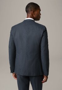 Giacca da uomo scura con una texture marcata, dal design aderente e chiusura a due bottoni, caratterizzata da un rever a vista e un motivo sottile, vista dal retro.