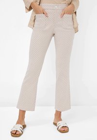 Lichte, gemusterde uitlopende broek in beige met een gestructureerd oppervlak en twee voorkruiszakken; gecombineerd met witte sandalen met banden.