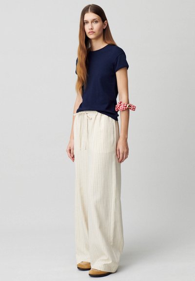 T-shirt a maniche corte blu navy abbinato a pantaloni larghi a righe crema, con cintura coulisse e un accento a quadretti rossi sul braccio.