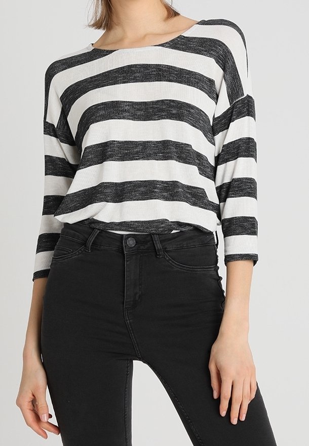 Femme portant un haut à manches trois-quarts blanc à rayures horizontales noires, rentré dans un jean skinny noir taille haute.