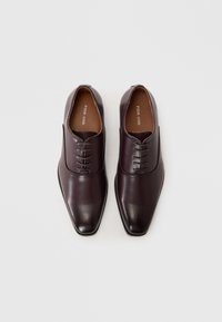 Chaussures habillées en cuir marron avec une finition lisse, bout pointu et un design à lacets à six œillets. L'intérieur présente une semelle intérieure marron clair.