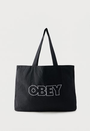 Black fabric tote bag with long handles, featuring the word "OBEY" in large, bold white outlined letters on the front.