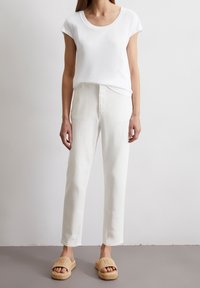 Vit t-shirt med rund hals, lös passform, kombinerad med vita höga byxor. Skorna är bruna vävda slidesandaler med logotypdetalj.