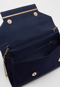 Borsa a mano in suede blu navy con un accento in metallo color oro nella parte superiore, dotata di una tasca con zip all'interno e chiusure a pressione sulla parte anteriore.