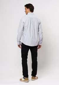 Cămașă cu dungi albă și albastră, cu mâneci lungi. Asortată cu pantaloni negri și adidași bej. Vedere din spate.