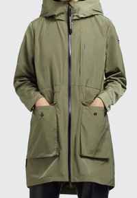 Olivgrön vattentät jacka med huva, främre dragkedja och stora fickor med lappar. Har en mjuk textur och en avslappnad passform.