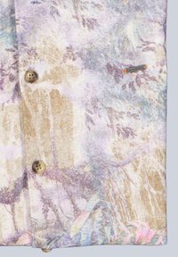 Light-colored fabric with muted abstract floral pattern, two brown buttons, and a small rectangular metal brand tag stitched near the edge.