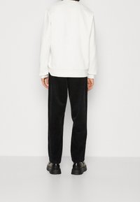 Vit sweatshirt med rund halsringning, kombinerad med svarta kordbyxor. Svarta skor synliga längst ner. Enkel och avslappnad design.