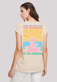 Beige Kurzarm-T-Shirt mit einem bunten grafischen Design eines Sonnensymbols, Wellen und Text auf der Rückseite in Orange-, Pink- und Blautönen.