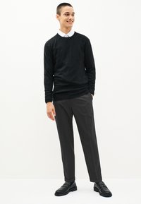 Čierny sveter s okrúhlym výstrihom, doplnený tmavosivými spoločenskými nohavicami. Oblečenie je dokončené čiernymi topánkami bez šnúrok.