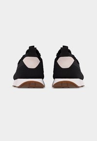 Ζευγάρι μαύρα αθλητικά παπούτσια με λευκές και καφέ σόλες, εμφανιζόμενα από πίσω σε απλό λευκό φόντο.