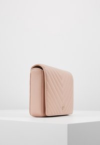Borsa a tracolla in pelle trapuntata rosa con pattina, dotata di un accento in tono oro e un motivo geometrico a zigzag. Forma rettangolare orizzontale.