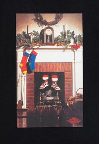 White and red sneakers with black accents on a brick fireplace, adorned with green garland, stockings, and a clock above.