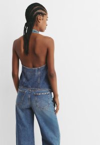 Denim halter top z odprtimi hrbtom, z prilegajočo zasnovo in kontrastnim svetlejšim denim pasom, v kombinaciji z širokimi hlačami in žeščenimi žepi.