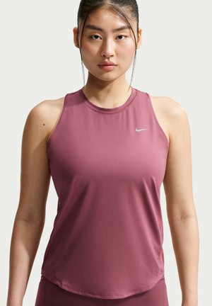 Giovane donna con capelli scuri raccolti indossa una canotta sportiva malva con un piccolo logo Nike sul petto, rivolta in avanti.