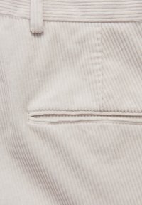 Manchester-tyg i offwhite färg, med vertikal ribbad struktur, en liten påsficka och sydda detaljer nära midjebandet.