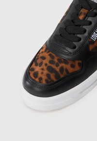 Detalus juodo sportinio bato, su ruda leopardine zomšos apdaila ir storu baltu padu, vaizdas ant vienspalvio fono.
