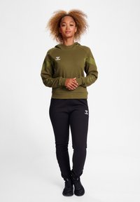 Olive green hoodie with a drawstring hood, black joggers, and athletic shoes. Features logo and contrasting sleeve patterns.