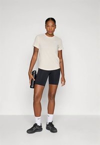 Heledat beež värvi spordisärk, mustad rattapüksid, mustad spordijalatsid ja valged sokid Nike logoga. Hoidmas musta joogipudelit.