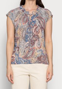 Kortärmad blus med ett paisleymönster i nyanser av blått, rött och beige, med en rynkad halsringning och knytdetalj.